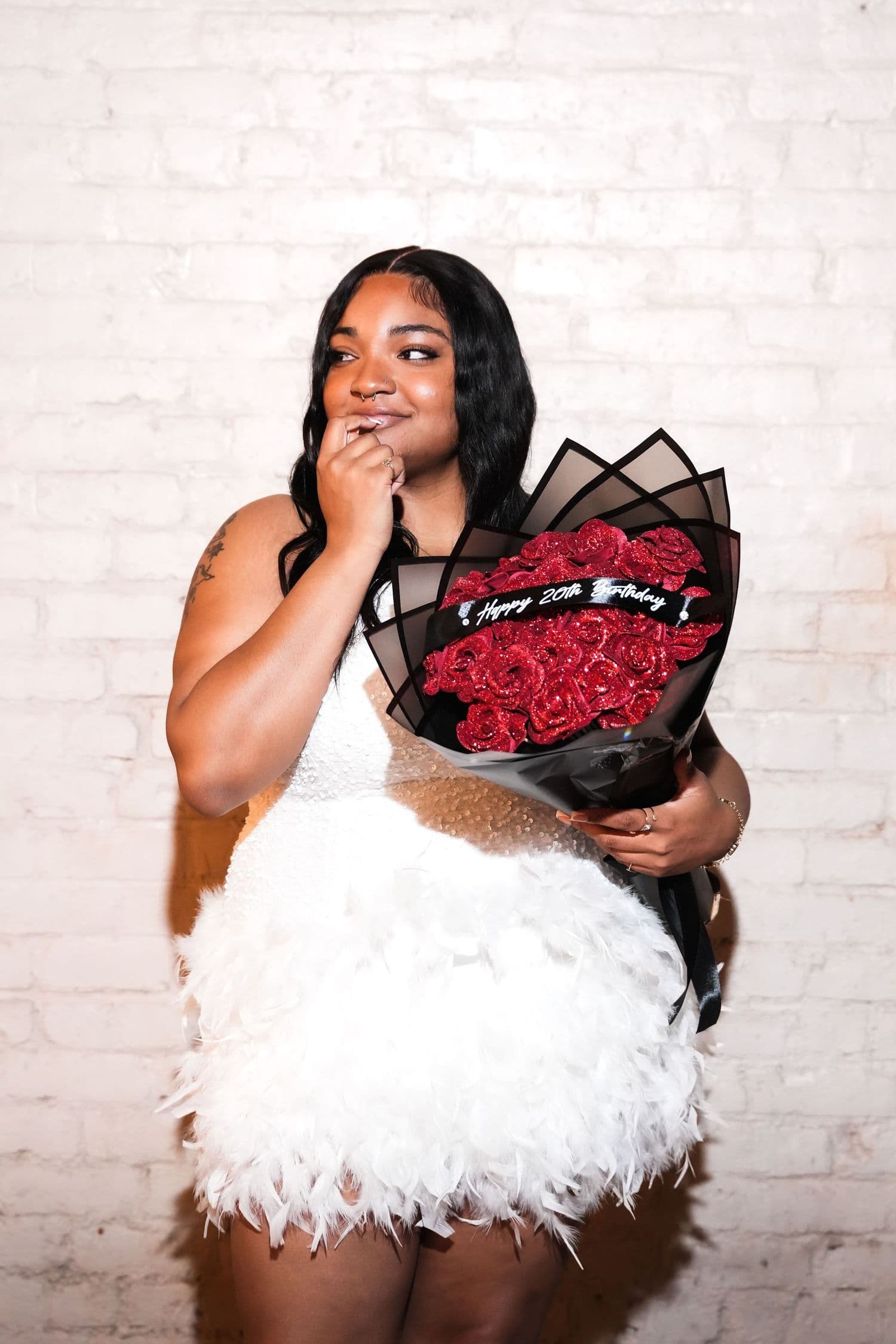 Birthday portrait in a white feather dress with red roses against a white brick wall